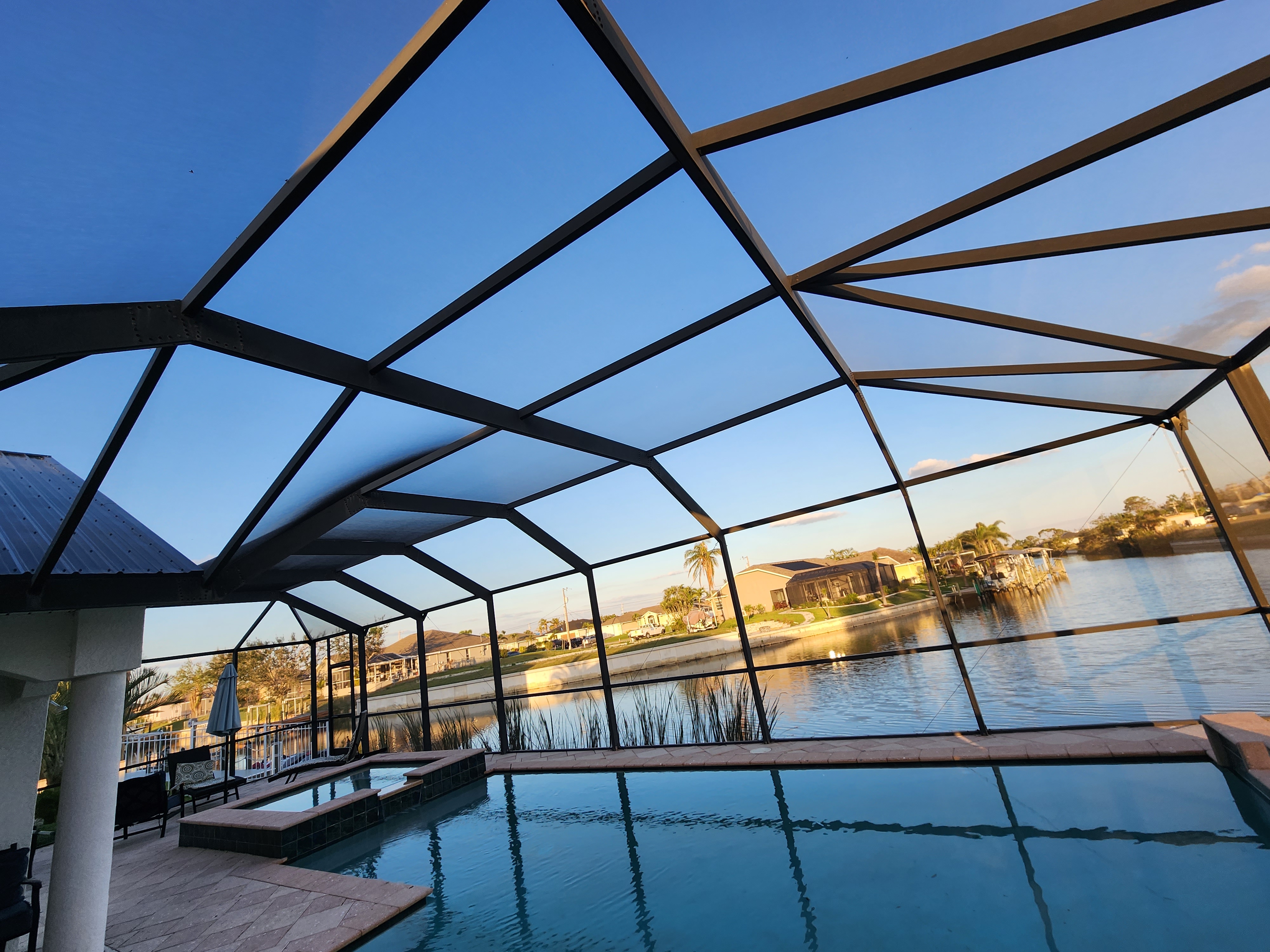 Restored waterfront pool cage with dark bronze aluminum frame overlooking a canal at sunset